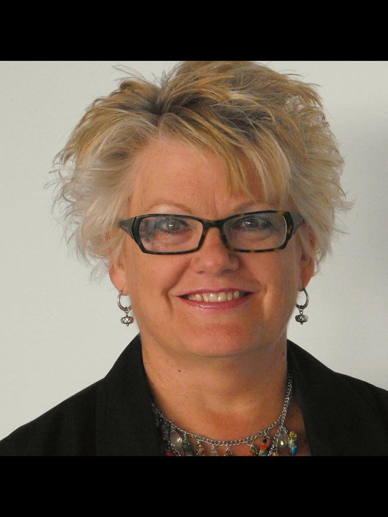 Kathleen Woodcock smiling, wearing glasses and a black jacket